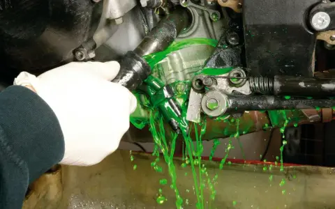Mano con guanto bianco che scollega un tubo, facendo fuoriuscire liquido verde brillante per il cambio del liquido radiatore.