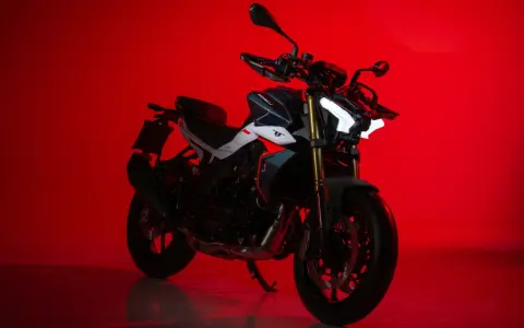 La Benelli TNT 500, con il suo design aggressivo e i fari a LED luminosi, si staglia su uno sfondo rosso acceso, pronta a conquistare la strada.