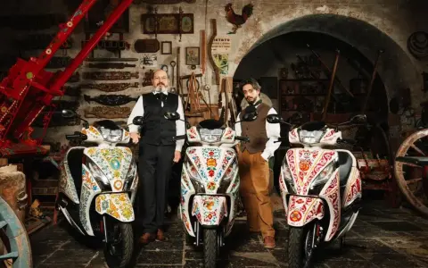 Due uomini in abiti tradizionali posano con tre scooter decorati. Uno scooter non si accende il quadro, ma l'arte sui veicoli è vibrante.