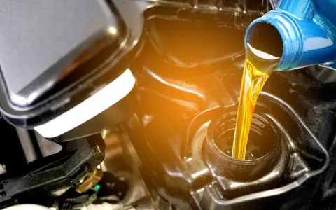 Olio giallo versato da una bottiglia blu in un motore. La differenza tra olio sintetico e minerale è fondamentale per la salute del motore.