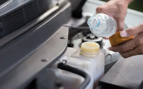 Mani versano acqua nel serbatoio del liquido di raffreddamento dell'auto, assicurandosi che ci sia acqua nel radiatore.