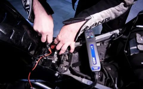 Mani che collegano un caricabatterie Exide a una batteria di moto. La batteria non tiene la carica, quindi si prova a ricaricarla.