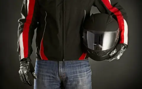 Motociclista con giacca nera e strisce rosse, jeans e casco nero. Le giacche ad uso motociclistico sono pronte per la strada.