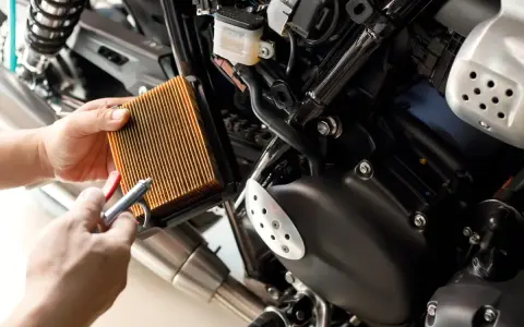 Mani puliscono il filtro dell'aria di una moto con aria compressa. Un filtro pulito è essenziale per il corretto funzionamento del motore, garantendo che a cosa serve il filtro dell'aria.