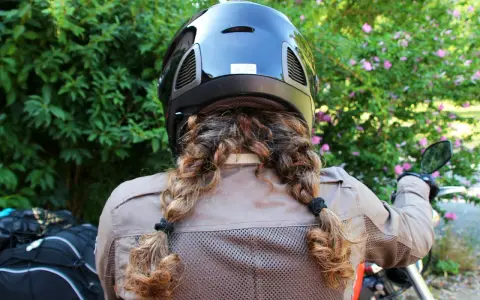 Donna con casco nero e capelli raccolti in due trecce, pronta a legare il casco alla moto.