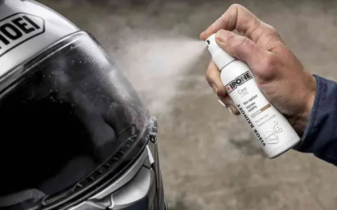 Mano spruzza spray idrorepellente sul casco Shoei. Il casco non deve essere pulito con benzina, ma con prodotti specifici per la visiera.