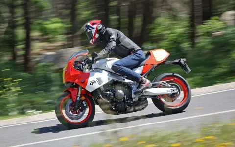 Un motociclista sfreccia su una Yamaha XSR900 GP, con il paesaggio sfocato dallo sfondo verde e giallo.