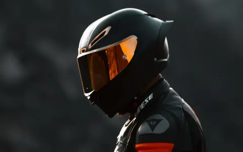 Casco da moto integrale nero con visiera arancione riflettente, pronto per la pista.