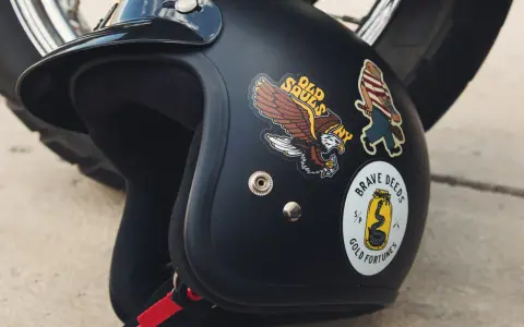 Casco nero con adesivi: un'aquila, un personaggio a strisce e un serpente in un barattolo. Si possono attaccare adesivi sul casco per personalizzarlo.