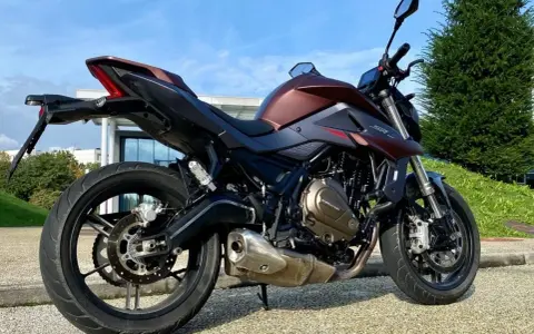 Moto SRK 700 color bronzo e nero, parcheggiata all'aperto con cielo azzurro e verde.