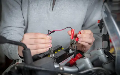 Mani che collegano i cavi a una batteria da moto ferma per ricaricarla.
