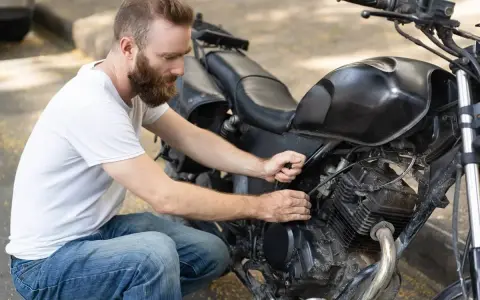 Uomo con barba lavora sul motore di una moto, forse per sostituire subito la batteria.