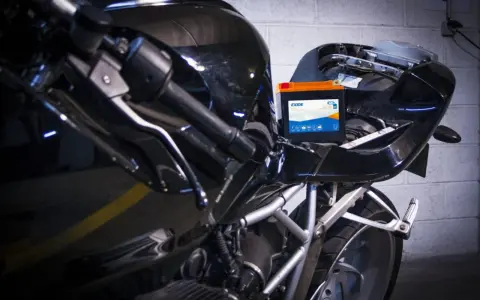 Una batteria nuova va caricata. La nuova batteria Exide è posizionata sul telaio di una moto nera lucida, pronta per essere collegata.