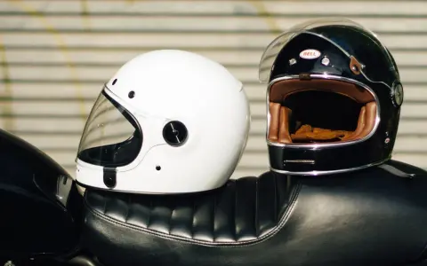 Due caschi integrali, uno bianco e uno nero, appoggiati sul sedile di una moto. Il peso del casco integrale è un fattore importante per il comfort.