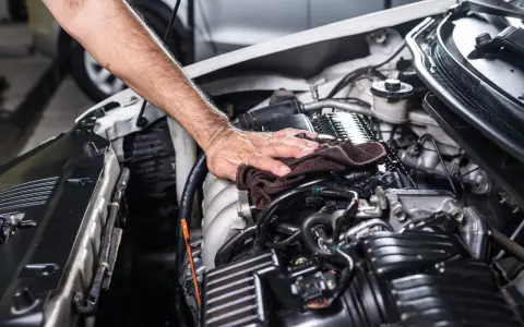 Mano che pulisce il motore dell'auto con un panno scuro, parte di un lavaggio motore accurato.