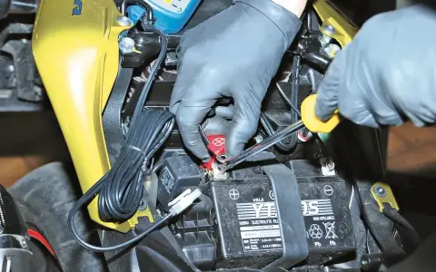 Mani guantate collegano un mantenitore di carica moto sempre collegato alla batteria.