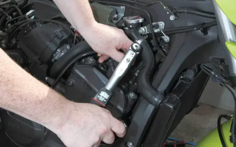Mani che usano una chiave dinamometrica per il cambio candele di una moto.