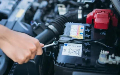Mano con chiave inglese che inizia a staccare batteria auto.