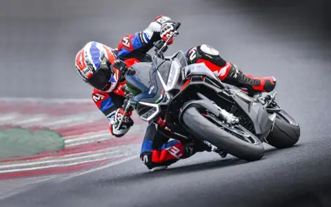 Un pilota in piega su una Aprilia Tuono 660 Factory, con tuta rossa e blu, affronta una curva su pista.