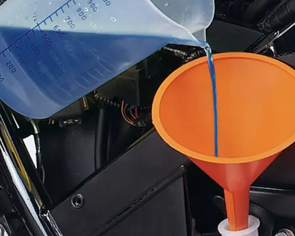 Versando liquido refrigerante blu in un imbuto arancione per diluirlo.