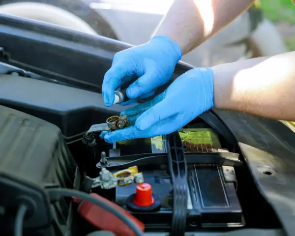 Mani con guanti blu puliscono i contatti arrugginiti della batteria rosso e nero dell'auto.