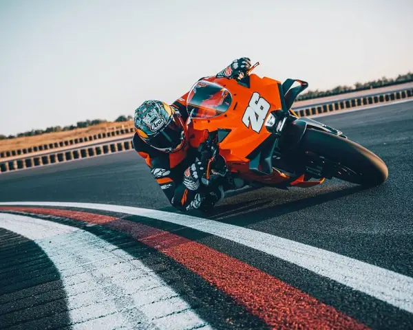 Un pilota con tuta arancione e casco decorato piega in curva su una KTM su una pista da corsa.