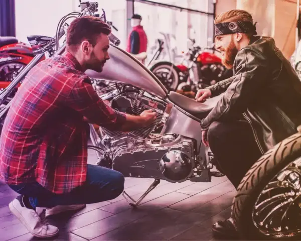 Due uomini esaminano un motore di moto custom. Uno mostra all'altro i dettagli, forse discutendo il costo della messa in strada della moto.