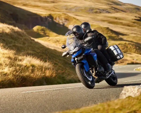 Coppia su una moto per due persone sfreccia su una strada panoramica tra colline dorate.