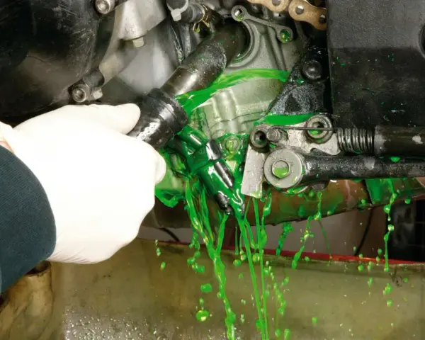 Mano con guanto bianco che scollega un tubo, facendo fuoriuscire liquido verde brillante per il cambio del liquido radiatore.