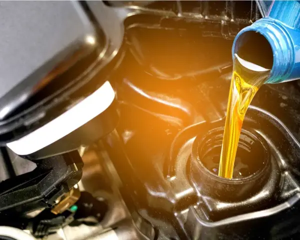 Olio giallo versato da una bottiglia blu in un motore. La differenza tra olio sintetico e minerale è fondamentale per la salute del motore.