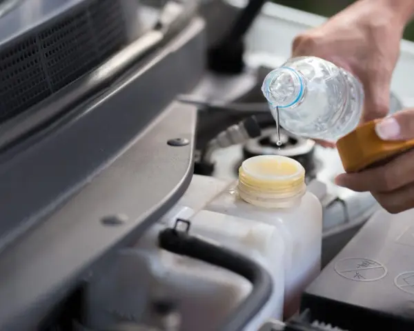 Mani versano acqua nel serbatoio del liquido di raffreddamento dell'auto, assicurandosi che ci sia acqua nel radiatore.