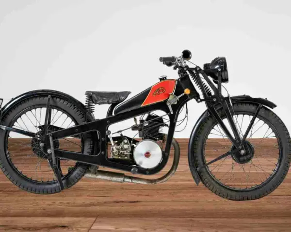 Una rara moto d'epoca, nera con serbatoio rosso e logo, su un pavimento di legno.