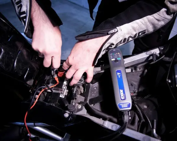 Mani che collegano un caricabatterie Exide a una batteria di moto. La batteria non tiene la carica, quindi si prova a ricaricarla.