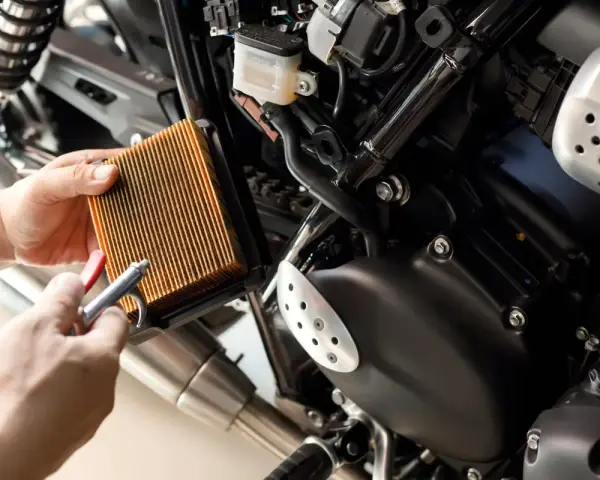 Mani puliscono il filtro dell'aria di una moto con aria compressa. Un filtro pulito è essenziale per il corretto funzionamento del motore, garantendo che a cosa serve il filtro dell'aria.