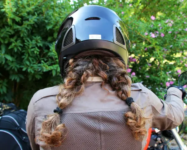 Donna con casco nero e capelli raccolti in due trecce, pronta a legare il casco alla moto.