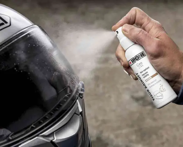 Mano spruzza spray idrorepellente sul casco Shoei. Il casco non deve essere pulito con benzina, ma con prodotti specifici per la visiera.