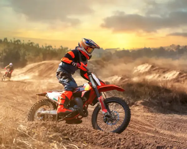 Un pilota di **enduro motocross** sfreccia su un terreno polveroso al tramonto, sollevando terra.