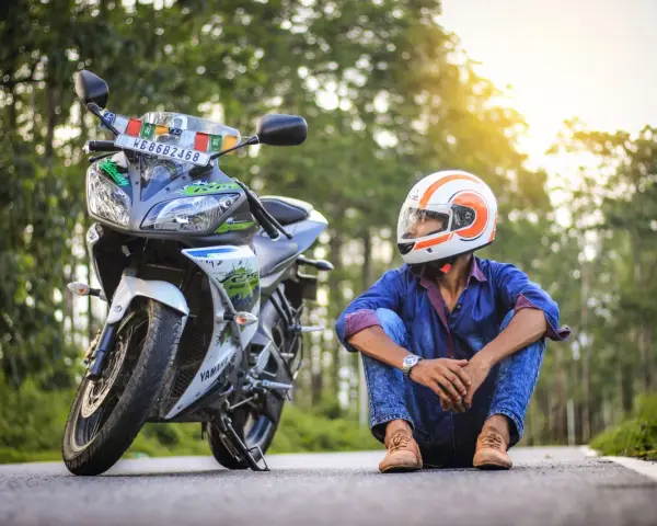 Giovane con casco da moto arancione e bianco, seduto accanto alla sua Yamaha. Spera di allargare il casco stretto per un viaggio più comodo.