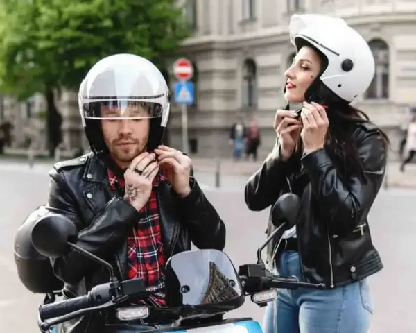 Coppia in moto, entrambi indossano un casco integrale. Lui con camicia a quadri, lei con giacca di pelle.