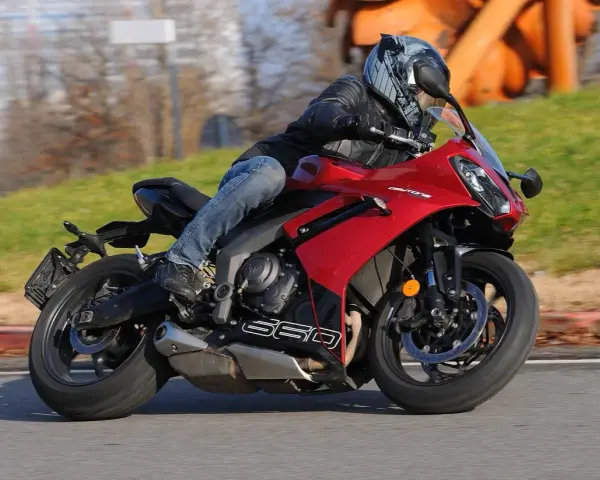 Un motociclista sfreccia su una moto sportiva rossa, tra le migliori moto sportive, con un casco moderno e jeans.