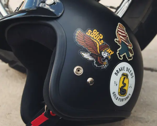 Casco nero con adesivi: un'aquila, un personaggio a strisce e un serpente in un barattolo. Si possono attaccare adesivi sul casco per personalizzarlo.