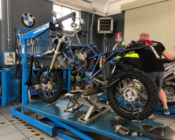 Officina BMW: moto smontata su sollevatore, in attesa del raffreddamento motore. Attrezzi e meccanico al lavoro.