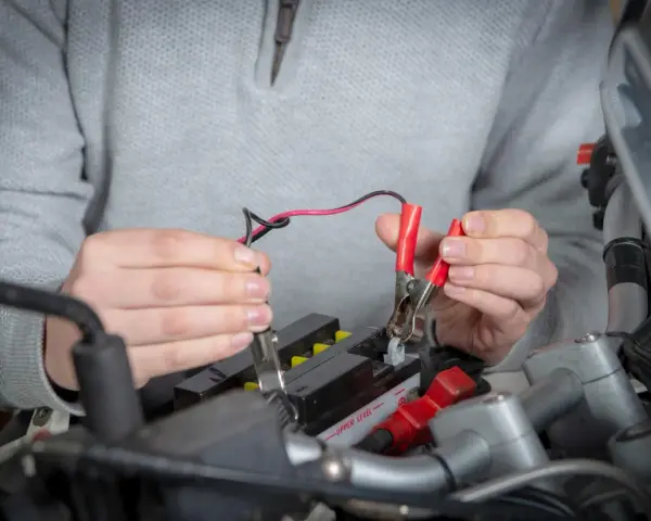 Mani che collegano i cavi a una batteria da moto ferma per ricaricarla.