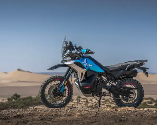 Moto blu e nera, perfetta per avventura e viaggi, posizionata su un terreno sabbioso con dune all'orizzonte.
