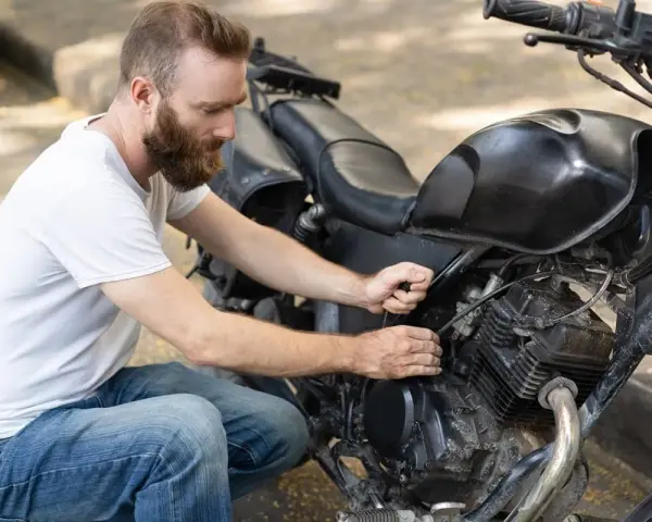Uomo con barba lavora sul motore di una moto, forse per sostituire subito la batteria.