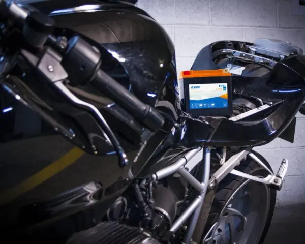 Una batteria nuova va caricata. La nuova batteria Exide è posizionata sul telaio di una moto nera lucida, pronta per essere collegata.