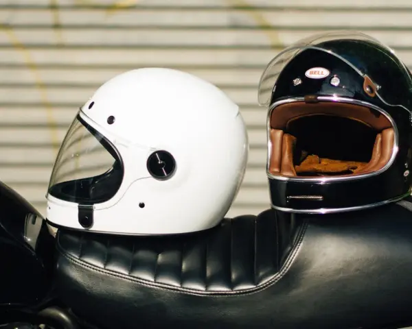 Due caschi integrali, uno bianco e uno nero, appoggiati sul sedile di una moto. Il peso del casco integrale è un fattore importante per il comfort.