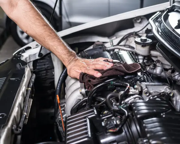 Mano che pulisce il motore dell'auto con un panno scuro, parte di un lavaggio motore accurato.