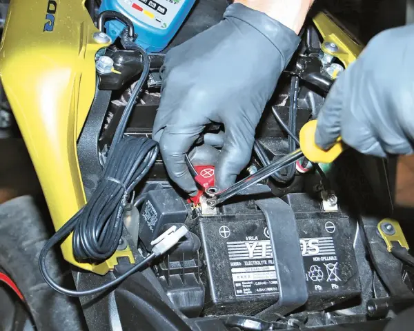 Mani guantate collegano un mantenitore di carica moto sempre collegato alla batteria.