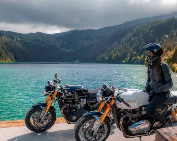 Due moto da enduro, una nera e una bianca, con una donna in sella, godono del panorama di un lago alpino.